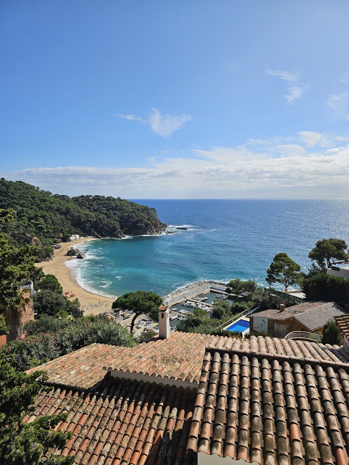 Stunning view of Costa Brava beach with clear blue waters and lush greenery from a rooftop perspective.
